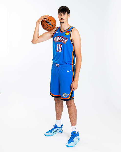 Aday Mara posa con un balón de baloncesto y la camiseta azul número 15 de Oklahoma City Thunder